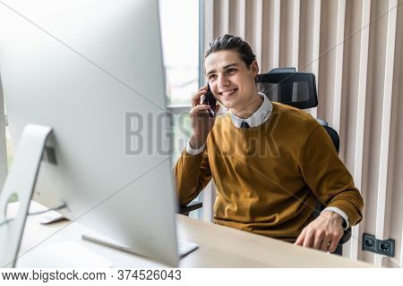 Smiling Businessman Talking On Mobile Phone While Working On Computer. Man Sitting At His Work Table