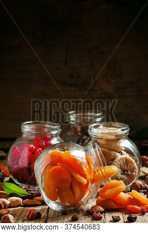 Dried Apricots In A Glass Jar On A Dark Wooden Background With Crumbled Nuts And Dried Fruits, Selec