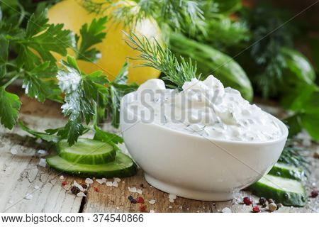 White Greek Sauce In White Bowl With Cucumber, Lemon Juice, Herbs And Spices On Old Wooden Table, Se