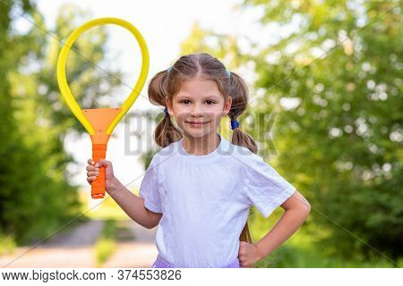 A Little Girl With Two Tails Holds A Tennis Racket In A Green Park.