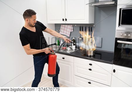 Man Using Fire Extinguisher To Stop Fire On Burning Cooking Pot In The Kitchen