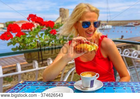 Happy Woman In Red Dress Heaving Breakfast With Croissant And Cappuccino In Italian Cafe. Scenic Lan