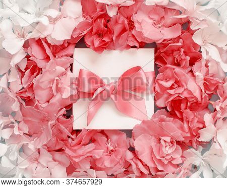 White Gift Box With A Bow Between Pink Flowers Top View