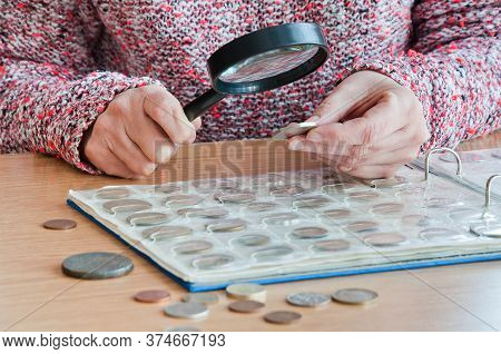 Woman-numismatist Views Coins From A Coin Album Through A Magnifying Glass