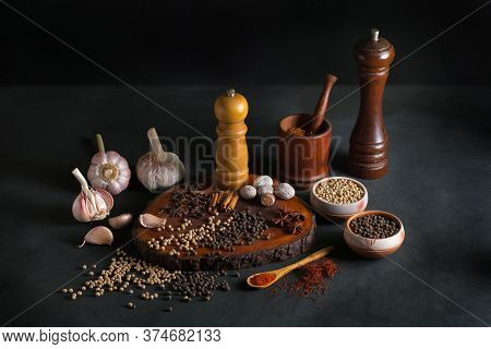 Still Life With Different Kind Of Spices Like Pepper, Nutmeg, Garlic, Cinnamon, And Paprika On A Bla