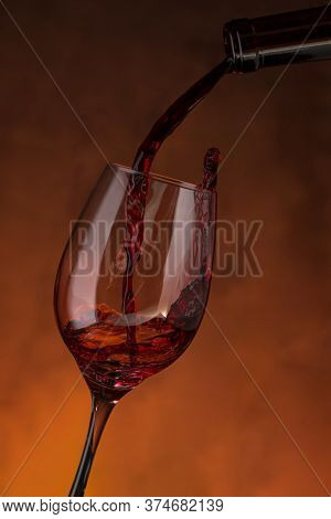 Bottle Filling A Glass With Red Wine On A Reddish Background