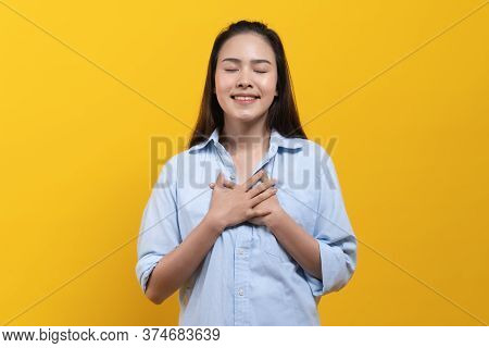 Appreciated Expression. Asian Woman Keeping Hands On Chest And Closing Her Eyes Isolated On Yellow B