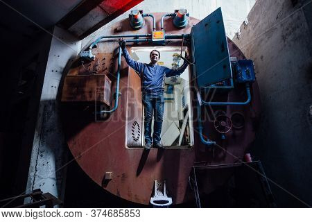 Man In Gateway Corridor Of Airlock Of Abandoned Bunker. Big Hermetic Door Illuminated By Red Lantern