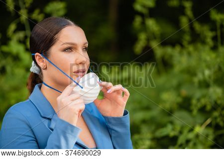 Beautiful Girl Puts A Medical Mask On Her Face On The Nature. Coronavirus And Covid-19 Protection