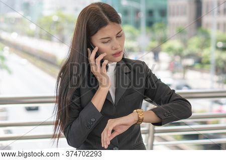Worried Asian Business People Looking At Wristwatch And Talking On Mobile With Colleagues That Late 