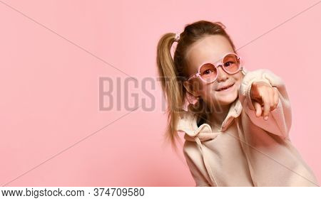 Smiling Little Girl Preschooler With Ponytale Looking Forward Pointing Index Finger At You. Close Up