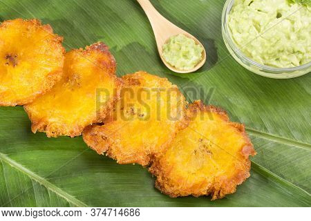 Patacón Fried Pieces Of Crushed Green Banana. Guacamole. On The Wooden Table (tostón, Tachino)