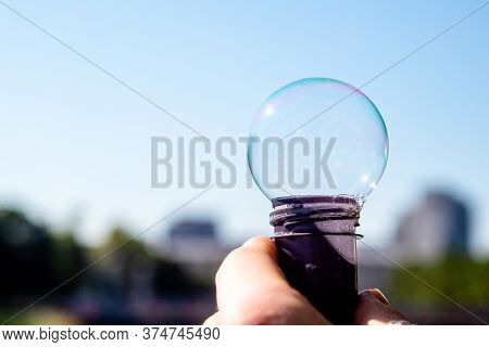 Round Soap Bubble Against The Sky. Human Hand Holding Bottle With Soap Bubble. Outside, Sunnny Day