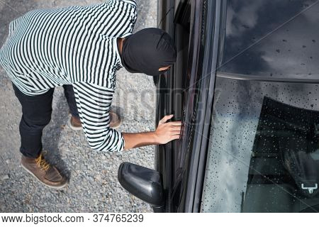 Thief In The Black Mask Looking In The Car And Trying To Break A Car Window To Steal A Car.
