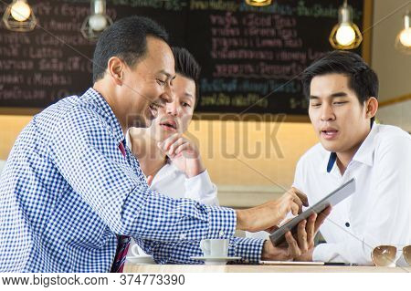 Asian Business Start Up Team Meeting In Cafe. Selective Focus On Man Holging Touchpad.
