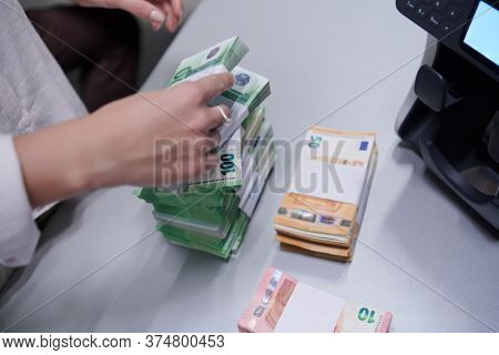 Bank employees using money counting machine while sorting and counting paper banknotes inside bank vault. Large amounts of money in the bank