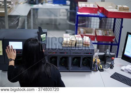 Bank employees using money counting machine while sorting and counting paper banknotes inside bank vault. Large amounts of money in the bank
