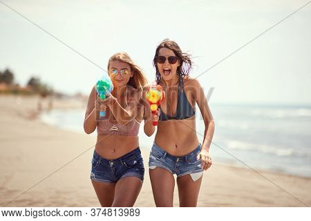 two women  pointing with water-guns on sandy beach