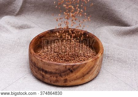 Raw Roasted Buckwheats Is Poured On Top Of Wooden Bowl On Cloth Surface. Russian Grechka. Organic He