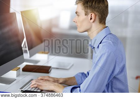 Young Successful Businessman Works With Computer, Sitting At The Desk In A Sunny Modern Office. Head