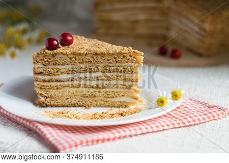 Piece Of Layered Creamy Honey Cake Decorated With Cherry On White Plate