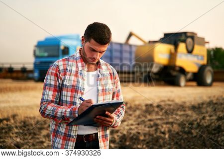 Farmer Controls Loading Wheat From Harvester To Grain Truck. Driver Holding Clipboard, Keeping Notes