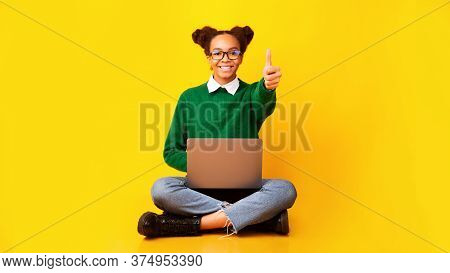Good Grade. Afro Teen Sitting On Floor With Laptop, Showing Thumbs Up Over Yellow Background, Copysp