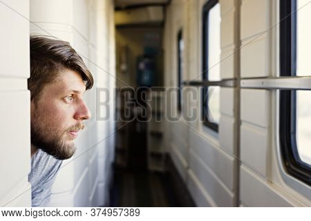 Handsome Young Caucasian Man With A Beard, Looks Outside Of The Trains Window, Looking Bored Or Tire