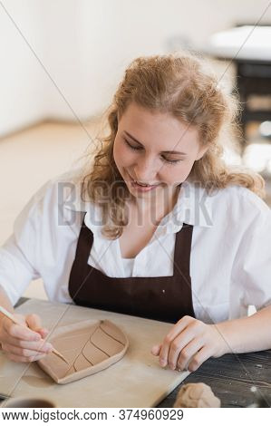 Womans Hand Making Clay Pottery On The Table With A Wooden Stick Instrument And Wooden Rolling Pin.