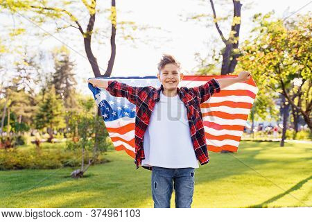 A Young Boy In A Red Plaid Shirt And White T-shirt Happily Standing In The Park With The Stretched U