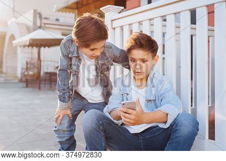 Two Attractive Caucasian Teenagers, Wearing Denim Jackets, Pants And White T-shirts Sitting Near Fen