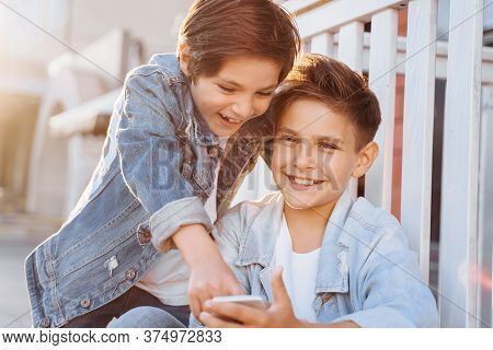 Two Attractive Caucasian Teenagers, Wearing Denim Jackets, Pants And White T-shirts Sitting Near Fen