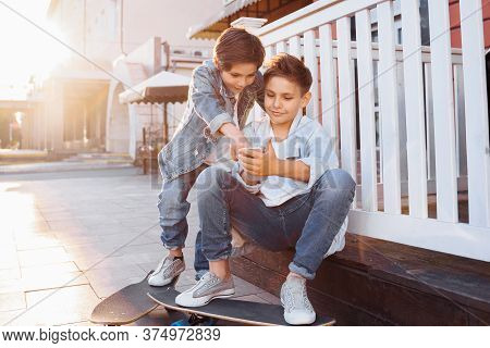 Two Attractive Caucasian Teenagers, Wearing Denim Jackets, Pants And White T-shirts Sitting Near Fen