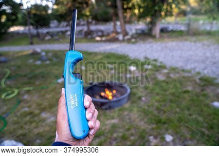 Livingston, Montana - July 3, 2020: Hand Holds Up A Bic Multipurpose Lighter, With A Campfire Defocu