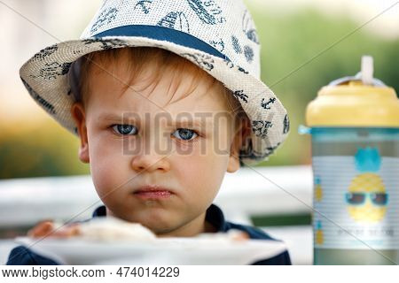 Angry And Displeased Little Blond Boy 3 Years Old Is Unwilling To Eat Bread With Cheese In The Garde