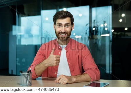 Portrait Of A Young Male Blogger Sitting At A Desk In The Office With A Camera And Talking Via Video