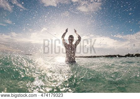 Silhouette Of Joyful Man Standing In Sea And Splashing Water Towards Camera. Sunny Day In Tropical D
