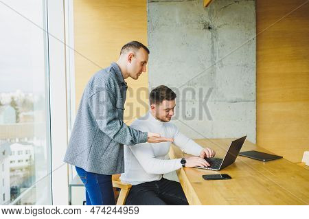 Two Male Colleagues While Working With A Laptop In The Office. Two Goal-oriented Entrepreneurs Colla
