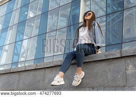 Resting Attractive Woman On City Street In Sunglesses. Young Woman In Youth Clothing On The City Str