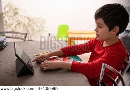 Side View Of A Caucasian 10 Years Child, Schoolboy Doing Homework, Sitting At Table And Watching Onl