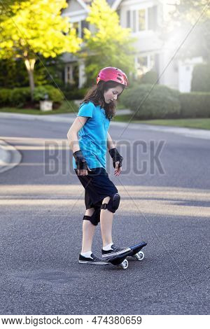 Young Girl Learning To Skateboard Or Ripstick On Street While Wearing Protective Gear During Bright 