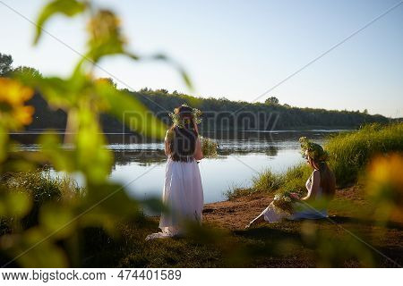 Adult Mature And Young Brunette Women In White Sundresses And Wreaths Of Flowers In Summer By Water 