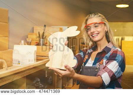 Cacausian Female Carpenter Smiles Admiring The Masterpieces Of Wooden Rabbit-shaped Furniture For Be