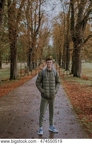 A Guy In A Jacket Stands On An Alley In The Park During The Fall Season. Portrait Oh Handsome Teen G