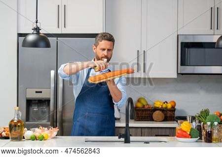 Man In Cook Apron Preparing Fish Salmon With Olive Oil At Home Modern Kitchen. Chef Is Cooking Fresh
