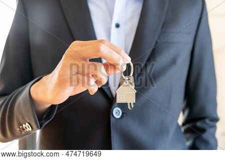 Home Agent, Broker Man In Suit Standing, Realtor Holding The House Key To Hand Over To New Homeowner