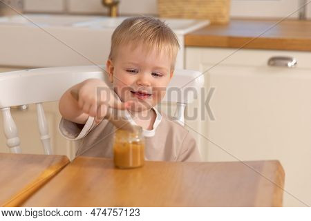 Happy Family At Home. Baby Boy Feeding Himself In Kitchen. Little Boy With Messy Funny Face Eats Hea