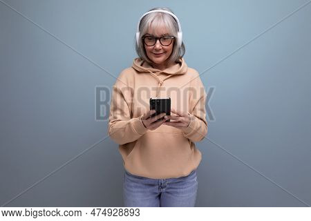 Stylish 60s Granny With Gray Hair Learns Again And Listens To Music With Headphones On Studio Backgr