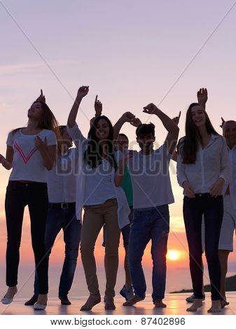 group of happy young people dancing and have fun on party in modern home bacony with sunset and ocean in background