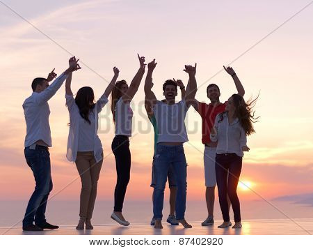 group of happy young people dancing and have fun on party in modern home bacony with sunset and ocean in background